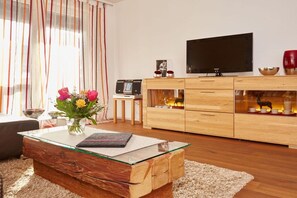 Uma sala de estar moderna com uma mesa de centro de vidro, armário de madeira, televisão de tela plana e objetos decorativos.