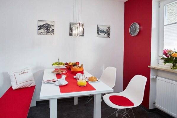 Uma sala de jantar com uma mesa branca, detalhes em vermelho e um relógio na parede.