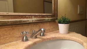 A bathroom with a marble sink, two faucets, a mirror, and a potted plant.