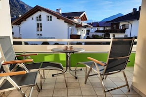Varanda com duas cadeiras e uma mesa, com vista para uma montanha e edifícios residenciais.