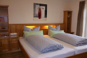 Uma cama de casal com roupa de cama xadrez, uma mesinha de cabeceira, um guarda-roupa de madeira e uma obra de arte pendurada na parede.