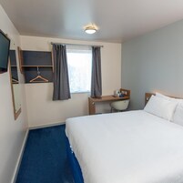 Habitación de hotel con cama, escritorio, silla, espejo y ventana con cortinas.