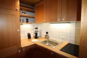 A kitchen with wooden cabinets, a stainless steel sink, a coffee maker, and a black induction cooktop. - Alpenflair Holiday Apartment 102 (Oberstdorf)