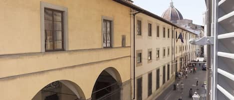 A street view with a building featuring arched windows and a dome in the background.