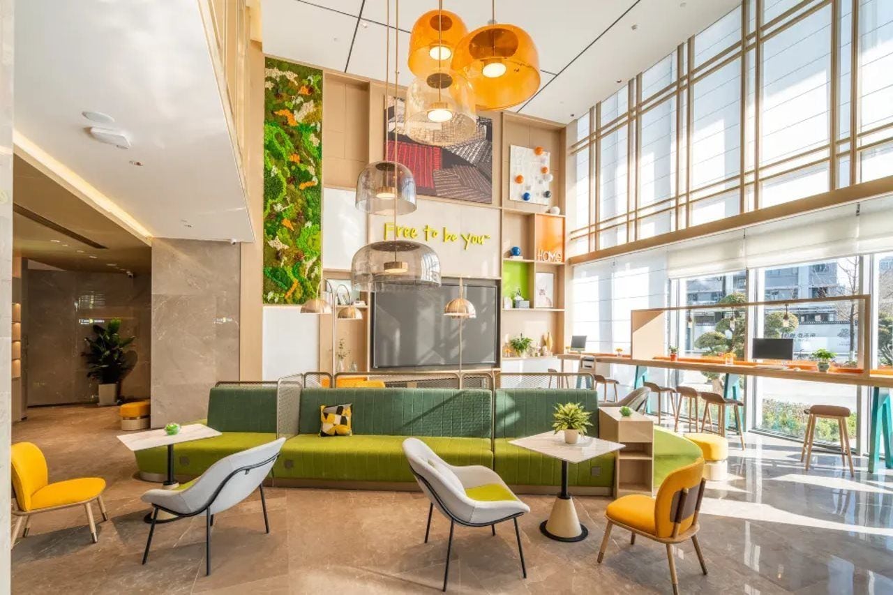 A modern interior with a green sofa, yellow chairs, a flat-screen TV, and a large window offering a view.