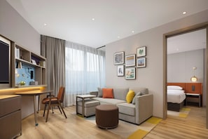 A modern hotel room with a dining area, a sofa set, a small table, and a bed. - Home2 Suites by Hilton Hangzhoudong Railway Station (Hangzhou)