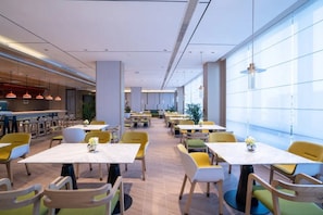 A modern dining area with multiple tables and chairs, a bar area, and large windows providing natural light. - Home2 Suites by Hilton Hangzhoudong Railway Station (Hangzhou)