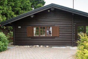 Eine Blockhütte mit der Aufschrift '22', einem Fenster mit Rollläden und einem gepflasterten Zugang.