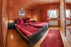 Ein Schlafzimmer einer Holzhütte mit einem Bett, Nachttischen, einem Fenster mit Vorhängen und einer Heizung.