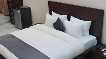 A modern hotel room with a large bed, a bedside table, a lamp, and a small cabinet.