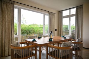 A dining area with a wooden table, chairs, and curtains. - Mastiff Select Riveria Resort, Igatpuri Road, Nashik (Nashik)