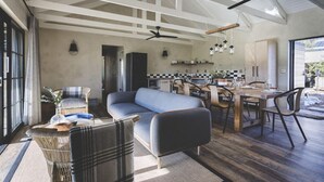 Amplia sala de estar con sofá, mesa de comedor y sillas, una cocina al fondo y un ventanal grande.
