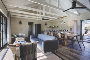 Amplia sala de estar con sofá, mesa de comedor y sillas, una cocina al fondo y un ventanal grande.