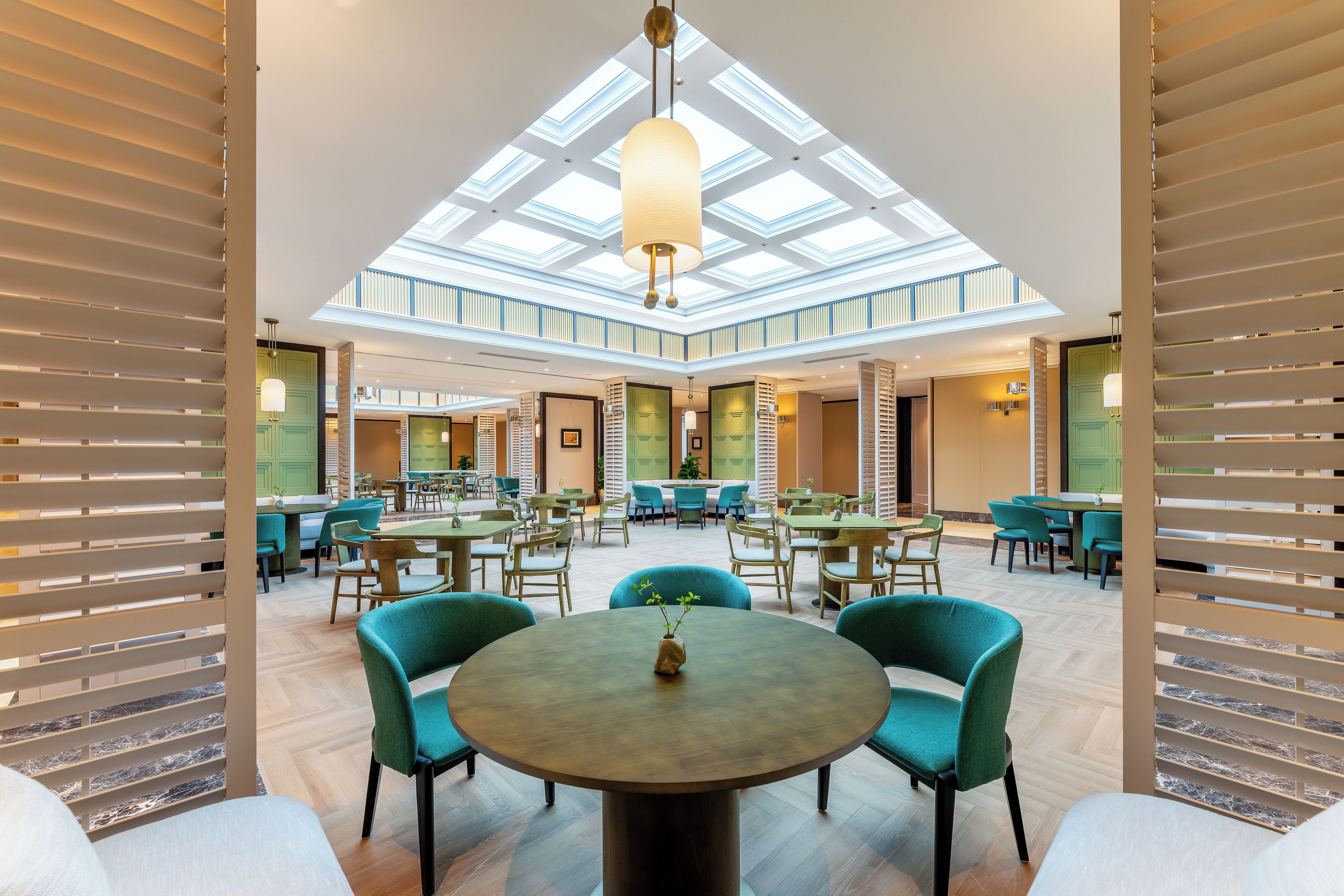 A spacious indoor area with a high ceiling and skylights, featuring multiple seating arrangements and a central round table with a vase.