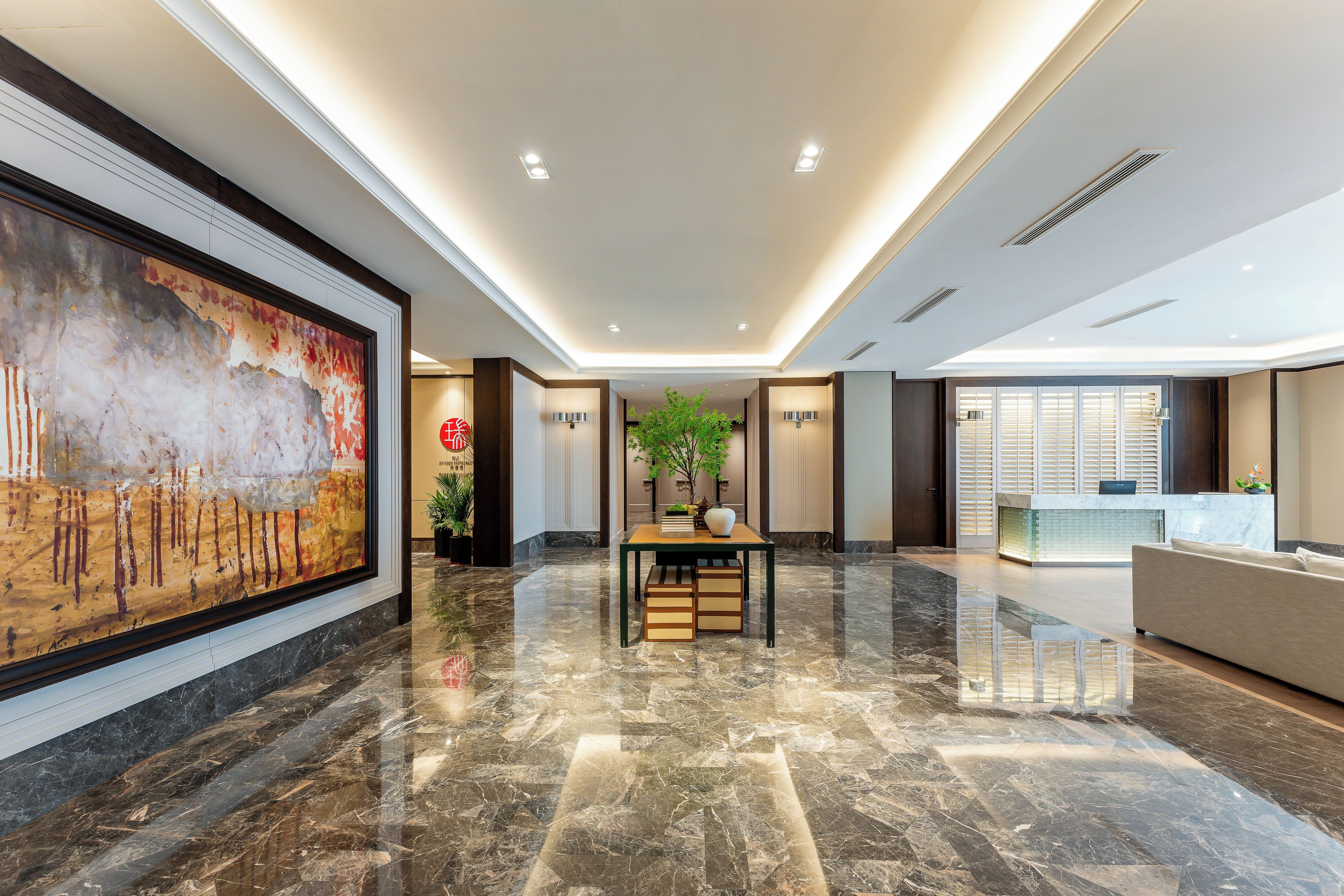 A spacious lobby with a marble floor, a reception desk, and a large abstract painting on the wall.
