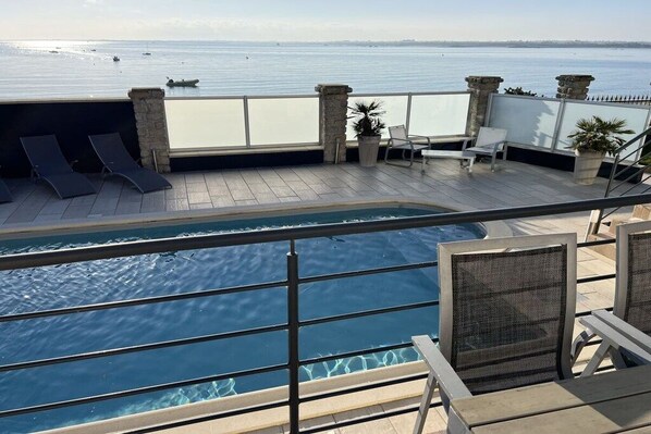 A pool area with lounge chairs and a view of the sea.