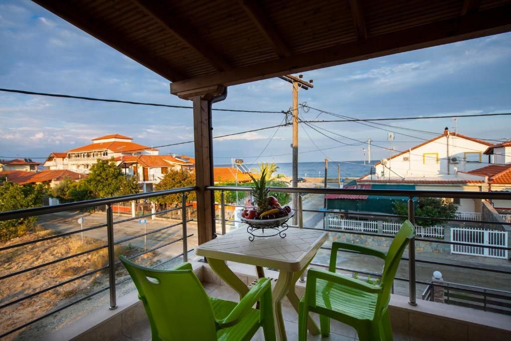 A balcony with a table and chairs, overlooking a coastal area with buildings and a clear sky.