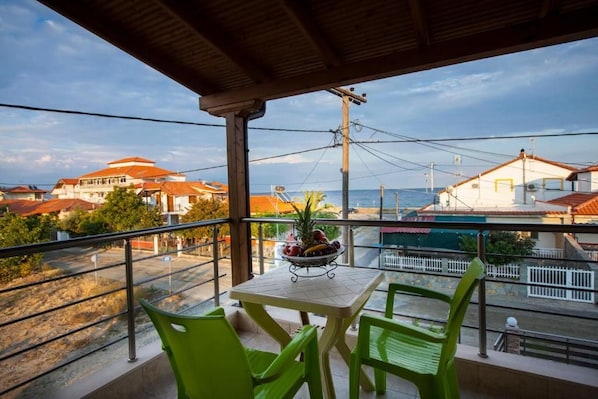 Uma varanda com mesa e cadeiras, dando vista para uma área costeira com edifícios e céu claro.