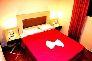 Quarto de hotel com cama, mesas de cabeceira e colcha vermelha.