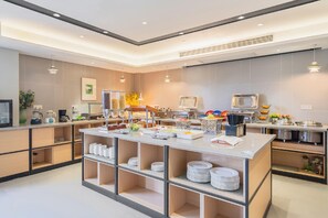 A modern kitchen with a buffet setup, including a central serving table with various food items and a coffee station. - Homeinn Selected (Wuxi)