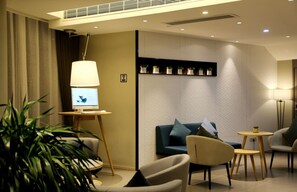 A modern living room with a sofa, chairs, a small table, a lamp, and a computer on a stand. - Homeinn Selected (Wuxi)
