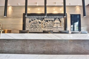 A reception area with a marble counter, a relief sculpture, and modern lighting fixtures. - Tian Sheng Ssaw Boutique Hotel Qi Dong (Nantong)