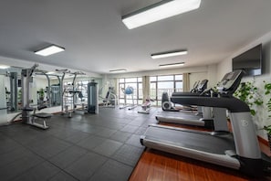 A gym with various exercise equipment, including treadmills and weight machines, and large windows providing natural light. - Tian Sheng Ssaw Boutique Hotel Qi Dong (Nantong)