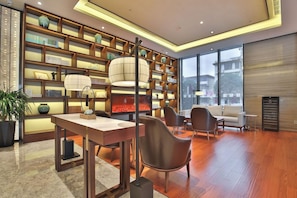 A modern interior with a wooden bookshelf, a dining area, and a seating space with a view through large windows. - Tian Sheng Ssaw Boutique Hotel Qi Dong (Nantong)