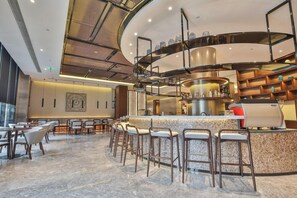 A modern bar area with a curved counter, multiple stools, and a kitchen area with a grill. - Tian Sheng Ssaw Boutique Hotel Qi Dong (Nantong)