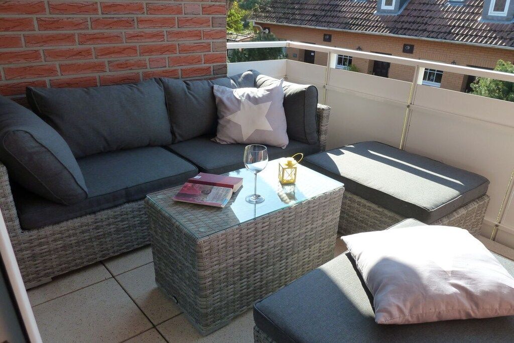 En balkon med en fletsofa, et glasbord og en polstret bænk.