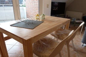 Uma mesa de jantar de madeira com um jogo americano preto, duas cadeiras com almofadas de pele e vista para uma parede de tijolos e uma janela.