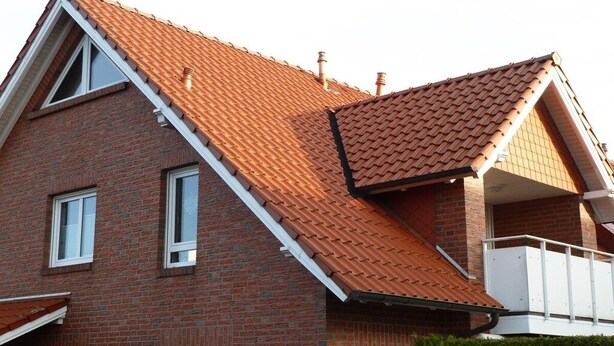 Ein zweistöckiges Backsteinhäuschen mit rotem Ziegeldach, weißen Fensterrahmen und einem weißen Balkon.