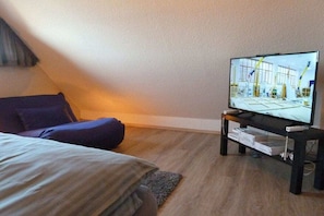 Quarto com uma cama, televisão sobre um suporte e janela.