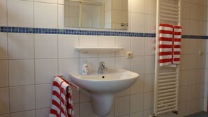 Ein Badezimmer mit einem weißen Waschbecken, einem Spiegel, einem Handtuchhalter mit gestreiften Handtüchern und einem Handtuchwärmer.