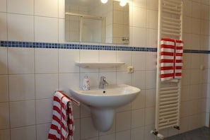 Casa de banho com uma pia branca, espelho, suporte de toalhas com toalhas riscadas e aquecedor de toalhas.
