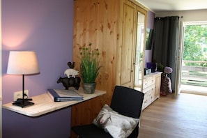 A room with a desk, chair, lamp, potted plant, and a wooden wardrobe. - Alpenflair Holiday Apartment 107 (Oberstdorf)