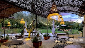 Un patio exterior con mesas y sillas, luces colgantes y vistas del paisaje circundante.