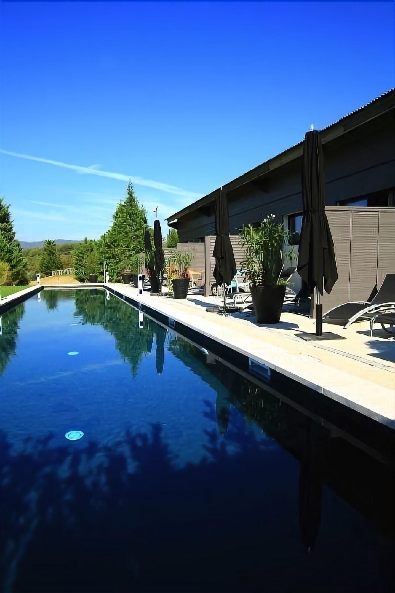 A swimming pool with lounge chairs and umbrellas, surrounded by potted plants and a modern building.