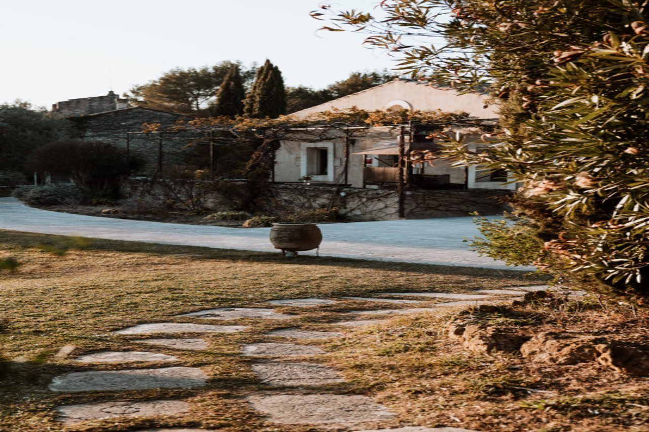 A stone pathway leading to a house with a garden and a large pot in the foreground.