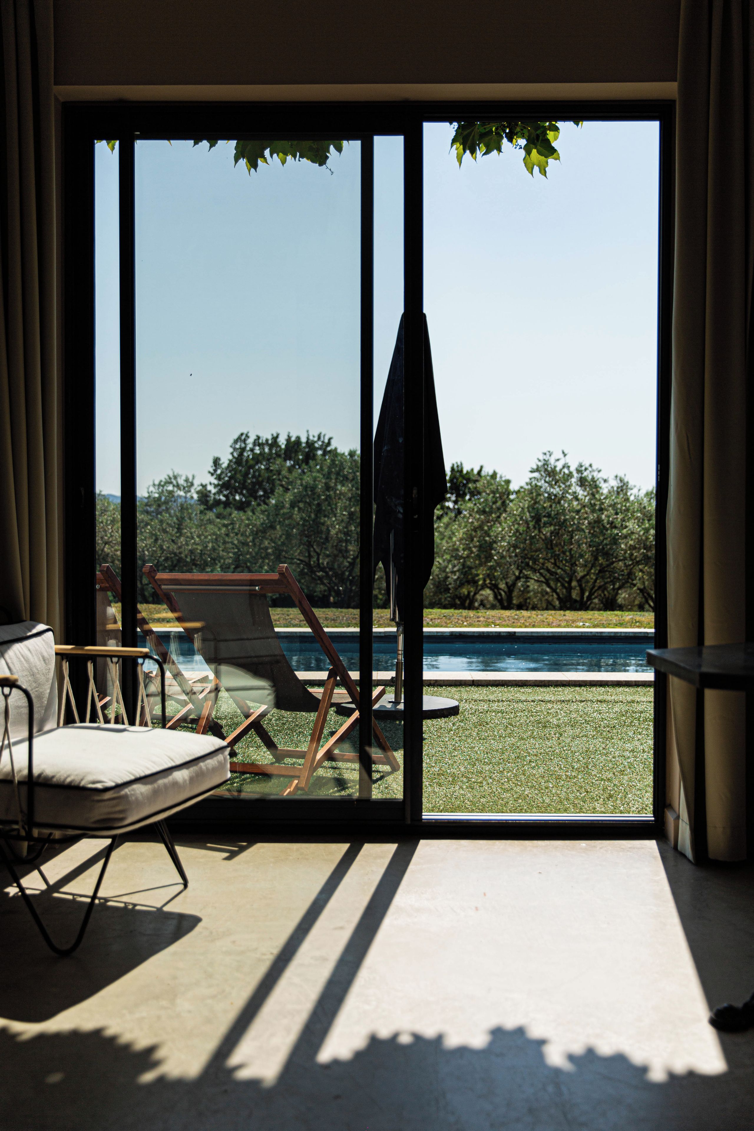 A room with a view of a swimming pool, a chair, and a table.