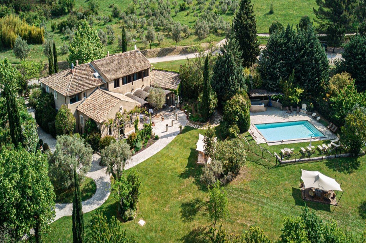 A large house with a swimming pool, surrounded by a well-maintained garden and a winding driveway.