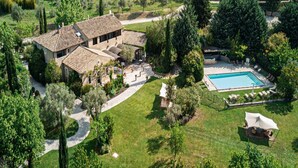Una casa grande con piscina, rodeada de un jardín cuidado y un camino de entrada sinuoso.