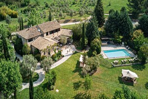 Una casa grande con piscina, rodeada de un jardín cuidado y un camino de entrada sinuoso.