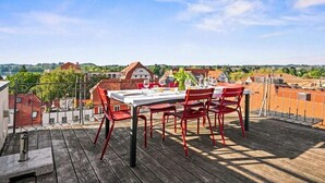 Une terrasse sur le toit, avec une table dressée pour le dîner, donnant sur un quartier résidentiel.