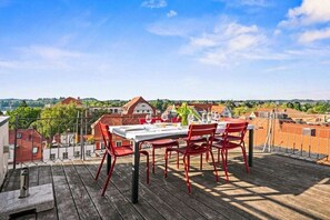 Une terrasse sur le toit, avec une table dressée pour le dîner, donnant sur un quartier résidentiel.