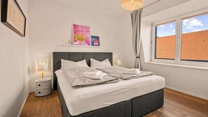 Une chambre à coucher avec un lit, des lampes de chevet, une fenêtre avec des rideaux et des œuvres d’art accrochées au mur.