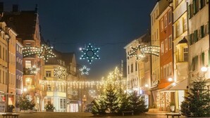 Une rue pavée, bordée de bâtiments de chaque côté, décorée de guirlandes lumineuses et d’ornements en forme d’étoiles.