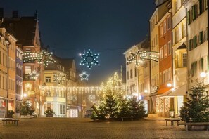 Une rue pavée, bordée de bâtiments de chaque côté, décorée de guirlandes lumineuses et d’ornements en forme d’étoiles.