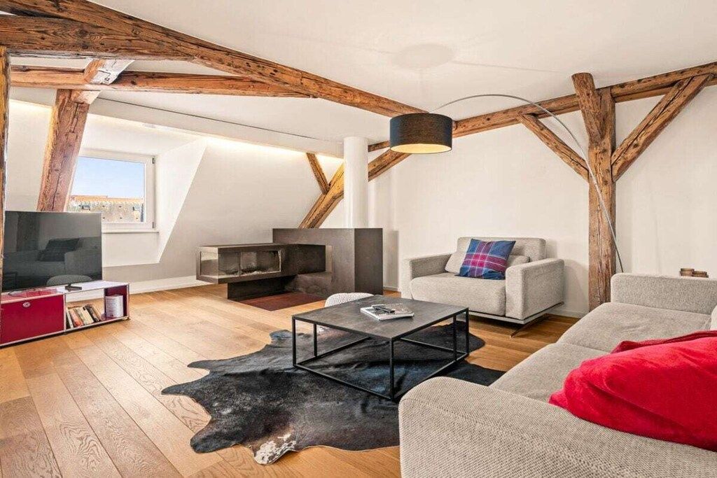 A loft-style living room with exposed wooden beams, a fireplace, a television, and a sofa.
