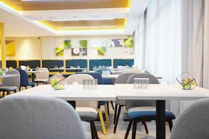A modern dining area with tables and chairs, a kitchen in the background, and decorative wall art. - Homeinn Selected (Xuzhou)